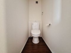 シンプルなデザインで清潔感のあるトイレ空間です。ホワイトを基調とした内装が明るい印象を与えます。床は木目調で落ち着いた雰囲気です。換気用の窓と通気口が設けられています。