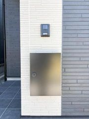 玄関にはTVモニター付きインターホンと宅配ボックスを備え、来訪者の確認や不在時の荷物の受け取りに便利です。白とグレーの外壁になじむスタイリッシュなデザインで、玄関まわりをすっきりと見せてくれます。