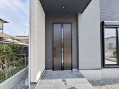 玄関はシンプルで洗練されたデザインが特徴です。落ち着いたカラーの玄関ドアが外観と調和しています。十分なスペースが確保されているアプローチ部分は屋根付きで、雨の日でも安心です。