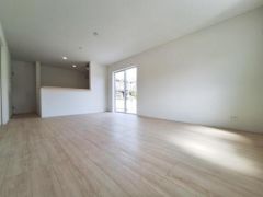 広々としたリビングには大きな窓から光が差し込みます。シンプルな内装が空間に開放感を与えています。明るいフローリングが印象的です。キッチンとリビングのつながりも魅力です。