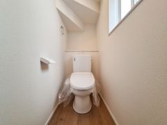 窓があり明るい印象のトイレ空間です。シンプルで落ち着いた内装が特徴的です。床は木目調で清潔感があります。換気しやすい設計です。スペースの使い方が工夫されています。