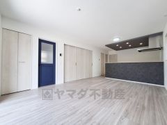 ナチュラルな色合いのフローリングが明るく広々とした空間を演出しています。キッチンとのつながりもスムーズなレイアウトです。収納扉やアクセントになる青いドアがポイントになっています。