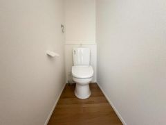 トイレはホワイトを基調とした清潔感のある空間です。床材の木目調がやさしい雰囲気を演出します。シンプルなデザインで掃除がしやすい造りです。ペーパーホルダーやタオル掛けも設置されています。