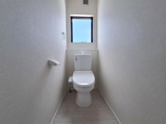 シンプルな内装で清潔感のあるトイレです。窓があり明るさと換気がしっかり確保されています。ペーパーホルダーや壁の色合いが落ち着いた印象です。トイレ空間が直線的で使いやすい設計です。
