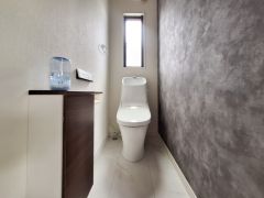 スリムな空間を活かしたトイレが設置されています。窓からの自然光が室内に明るさをもたらしています。壁面のアクセントカラーが印象的な雰囲気を演出しています。