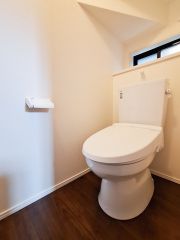 落ち着いた色合いの床材が特徴的なトイレです。壁や天井のシンプルなデザインが空間を引き立てています。自然光が入る窓付きで明るさを感じられます。清潔感のある白い便器が印象的です。