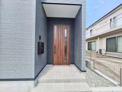シンプルで落ち着いた外観デザインの玄関が特徴です。木目調のドアがアクセントになっており全体的に統一感があります。玄関ポーチも広めでゆとりを感じられる仕様です。モダンな印象を与える玄関です。
