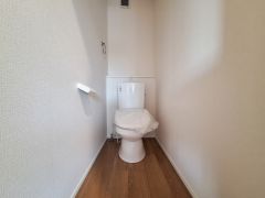 シンプルなデザインが特徴のトイレです。ナチュラルなフローリングが空間に温かみを与えています。壁面に手すりやペーパーホルダーが設置されています。コンパクトながらも使いやすい設計です。