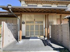 木の温もりを感じるデザインが特徴の玄関です。広めのアプローチ部分がすっきりとした印象を与えます。重厚な門構えと格子戸が和の雰囲気を引き立てています。