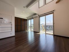 大きな窓から明るい日差しが差し込むリビングです。落ち着いた色合いのフローリングがモダンな印象を演出します。天井が高く開放感があります。収納スペースも確保されているのが特長です。