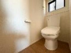 シンプルなデザインのトイレです。窓が設置されているため換気にも配慮されています。床は木目調で温かみのある印象です。壁際にはペーパーホルダーが配置されています。