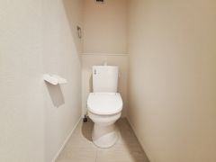 シンプルで清潔感のあるトイレ空間です。壁紙や床の色合いが明るく空間全体がすっきりとした印象になります。換気設備や窓が設けられており通気性にも配慮されています。収納スペースも確保しやすいレイアウトです。