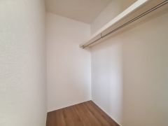 広々とした収納スペースが確保されています。天井まで伸びるハンガーパイプ付きで衣類の整理にも便利です。シンプルな内装で使いやすい空間になっています。床は木目調で清潔感があります。