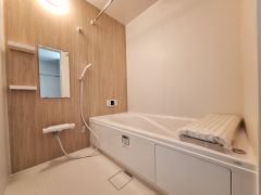 木目調の壁がアクセントの落ち着いたバスルームです。浴槽は広々としており手すり付きの設計です。明るい照明で視認性も高く清潔感を感じられます。