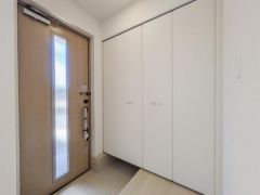 明るい木目調の玄関ドアが印象的です。壁面のクローゼットがすっきりとした収納スペースを確保しています。