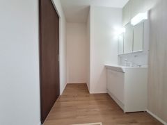 清潔感のある洗面台が備わった洗面所です。照明が二つあり明るい空間が広がります。収納スペースも充実しています。木目調の床が落ち着いた雰囲気を演出します。