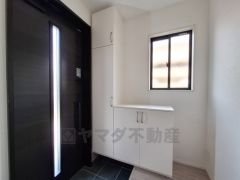 シンプルで清潔感のある玄関です。明るい採光窓があり心地よい光が差し込みます。収納スペースも確保されています。ダークカラーのドアが空間を引き締めます。