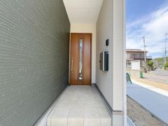 玄関はゆとりのあるスペース設計で使いやすい動線が確保されています。タイル貼りのアプローチが印象的で清潔感を感じられます。木目調のドアが外観に調和し落ち着いた印象を与えます。