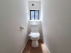 明るい窓付きのトイレ空間です。白を基調とした内装で清潔感があります。床は木目調で落ち着いた雰囲気です。換気がしやすく快適にご利用いただけます。無駄のないシンプルな設計です。