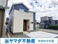 落ち着いたネイビーと可愛らしいベージュ、そして木目調の玄関ドアがバランスよく配されています。直線的なフォルムが存在感を引き立てています。前面にはすっきりと広々とした駐車スペースが確保されています。