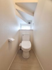 落ち着いた色合いの壁と床が特徴のトイレです。シンプルな設計で清潔感があります。奥行きも確保されているためゆったりと使用できます。無駄のないデザインが魅力です。清掃がしやすい空間となっています。